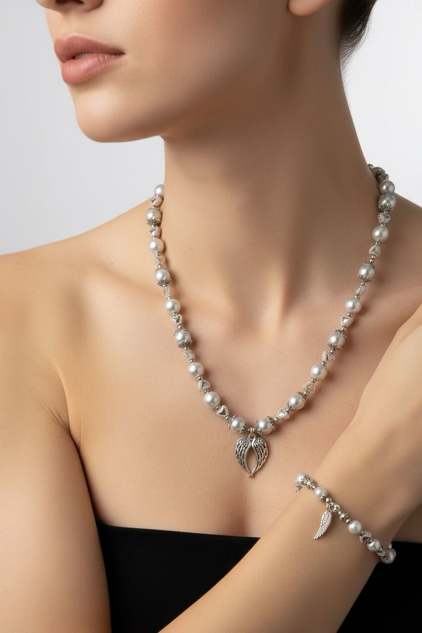 A silver-tone white glass pearl heart necklace and bracelet set with angel wing pendants is displayed on a model. 