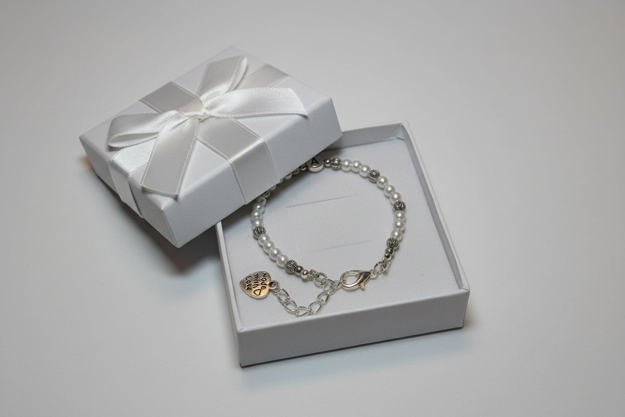 A beaded bracelet with white glass pearls and silver-toned metal beads, featuring a heart-shaped charm engraved with 'A' and a lobster clasp closure, shown in a white gift box.