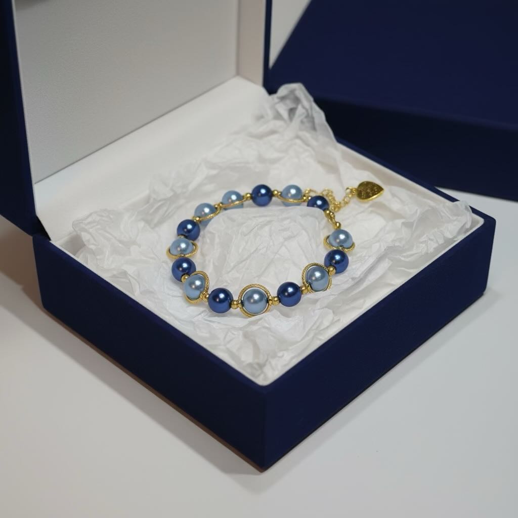 A pearl bracelet with dark royal blue and dark baby blue glass pearls and gold-toned settings, displayed inside an open navy blue jewelry box with white tissue paper.
