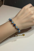 A close-up of a person's wrist wearing a pearl bracelet with dark royal blue and dark baby blue round glass pearls separated by small gold spacer beads, with a gold chain extender and clasp visible.
