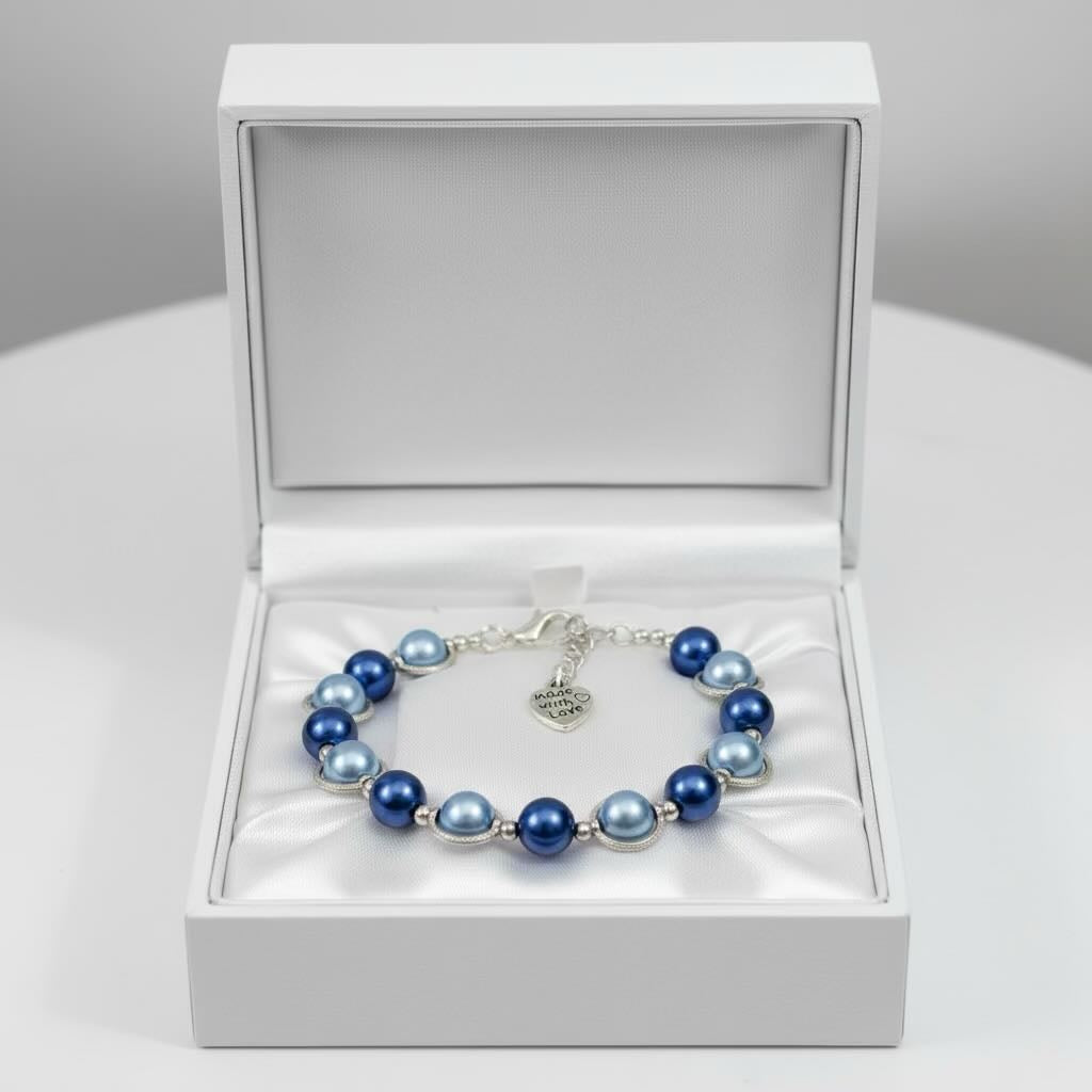 A beaded bracelet with blue and dark baby blue pearls and silver-toned metal links, displayed inside an open white jewelry box on a white surface.