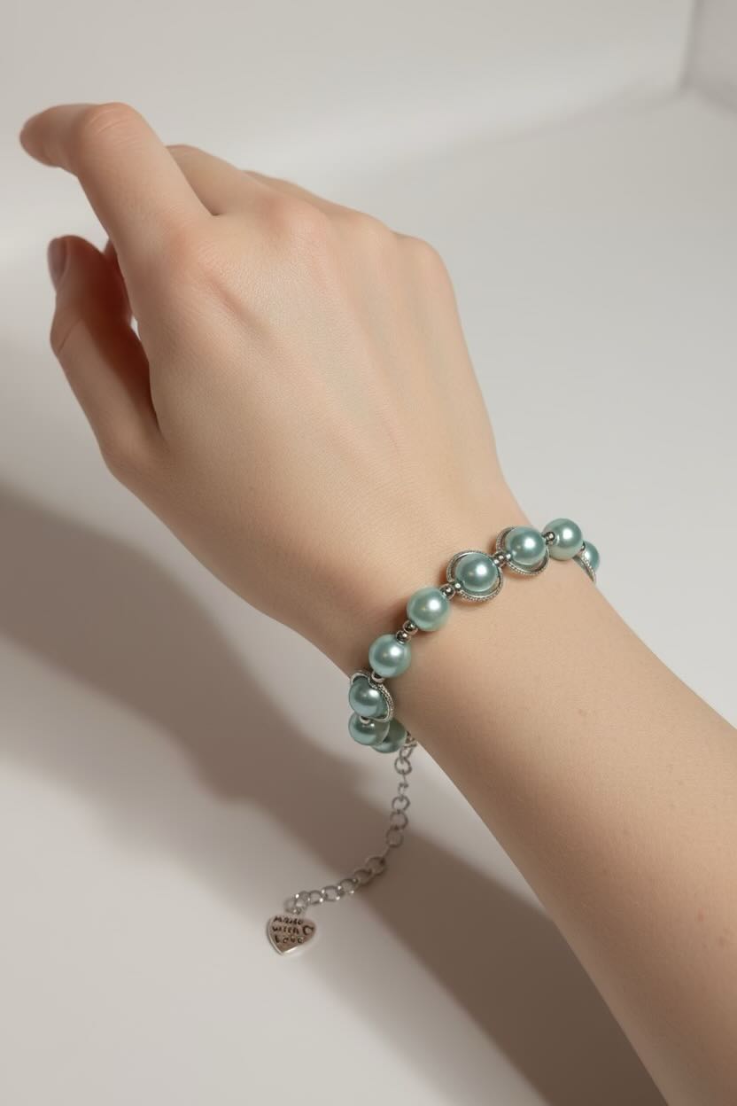 A close-up of a person's hand and wrist wearing a delicate bracelet made of aqua blue glass pearls and silver-toned metal links, with a small dangling heart charm.