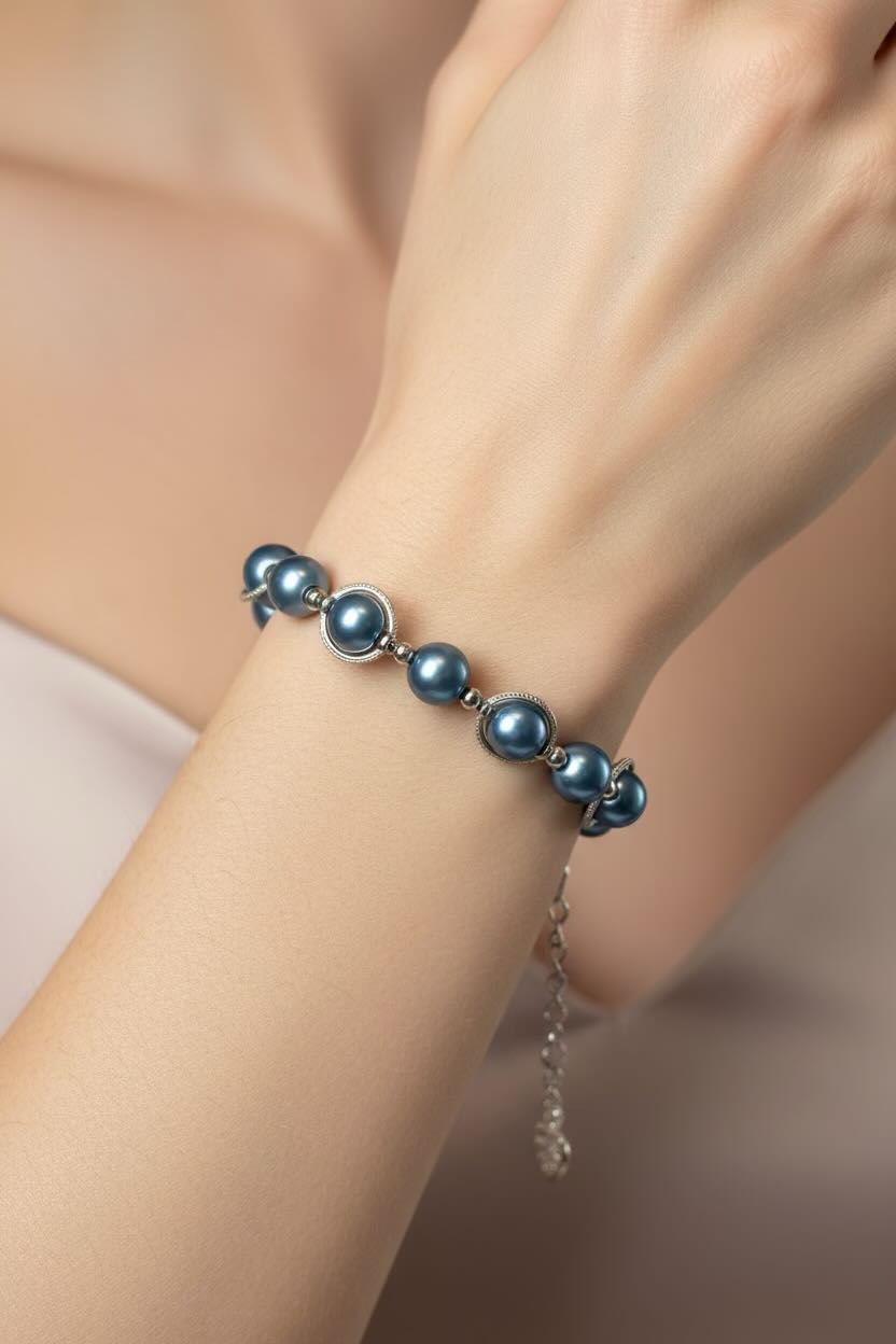 A close-up of a person's wrist wearing a bracelet made of teal blue pearls and silver-toned metal links, with a delicate silver chain extender hanging down.