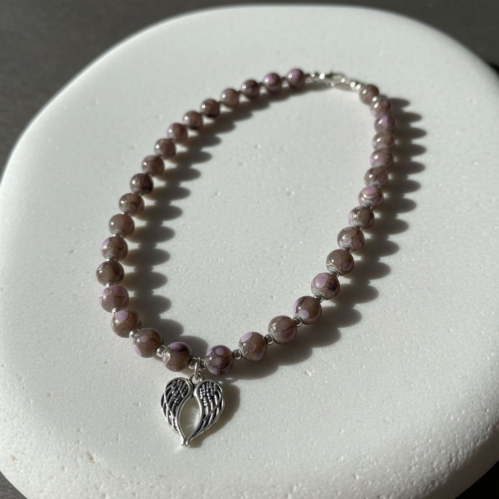 Necklace with purple beads and a silver angel wing charm on a white stone